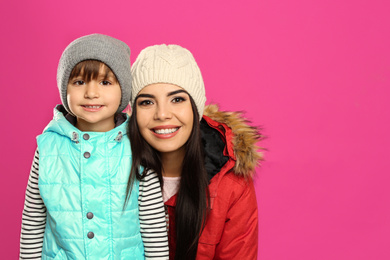 Happy mother and son in warm clothes on pink background. Winter vacation