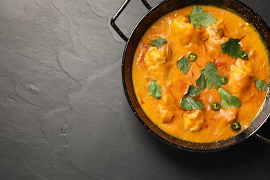 Photo of Tasty chicken curry with parsley and pepper on black textured table, top view. Space for text