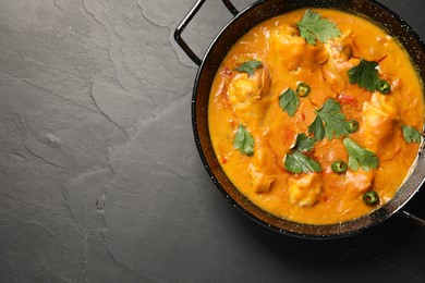 Tasty chicken curry with parsley and pepper on black textured table, top view. Space for text