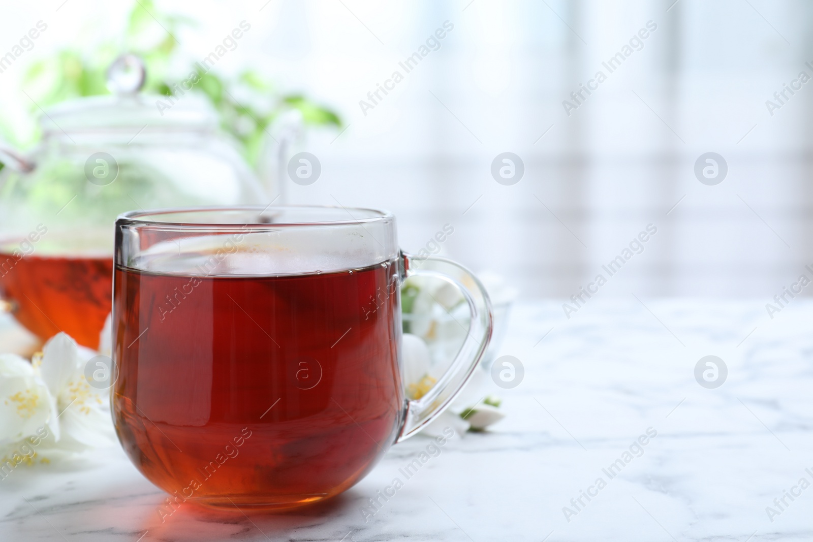 Photo of Cup of tea and fresh jasmine flowers on white marble table. Space for text