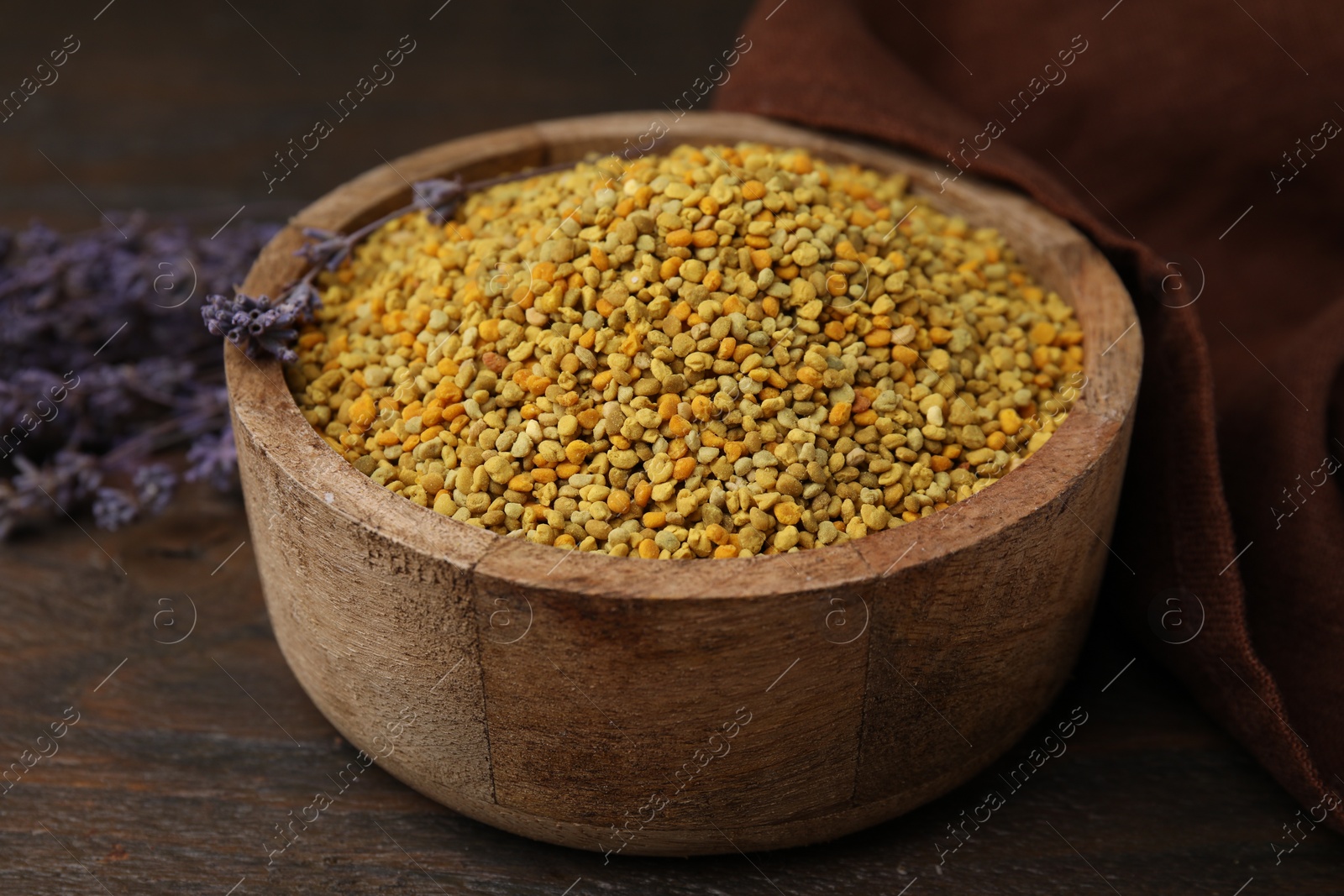 Photo of Fresh bee pollen granules in bowl and lavender on wooden table, closeup