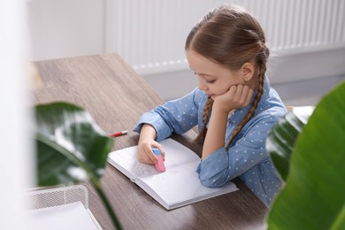 Girl erasing drawing in her book at wooden table in room