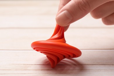 Photo of Woman playing with red spinning top at light wooden table, closeup