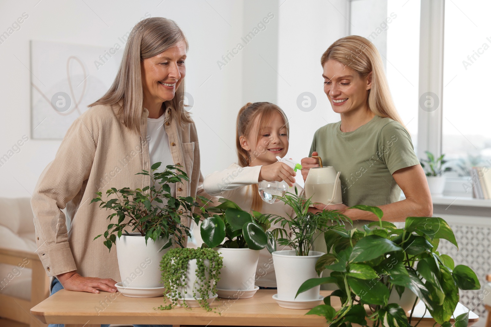 Photo of Three generations. Happy grandmother, her daughter and granddaughter watering houseplants at home