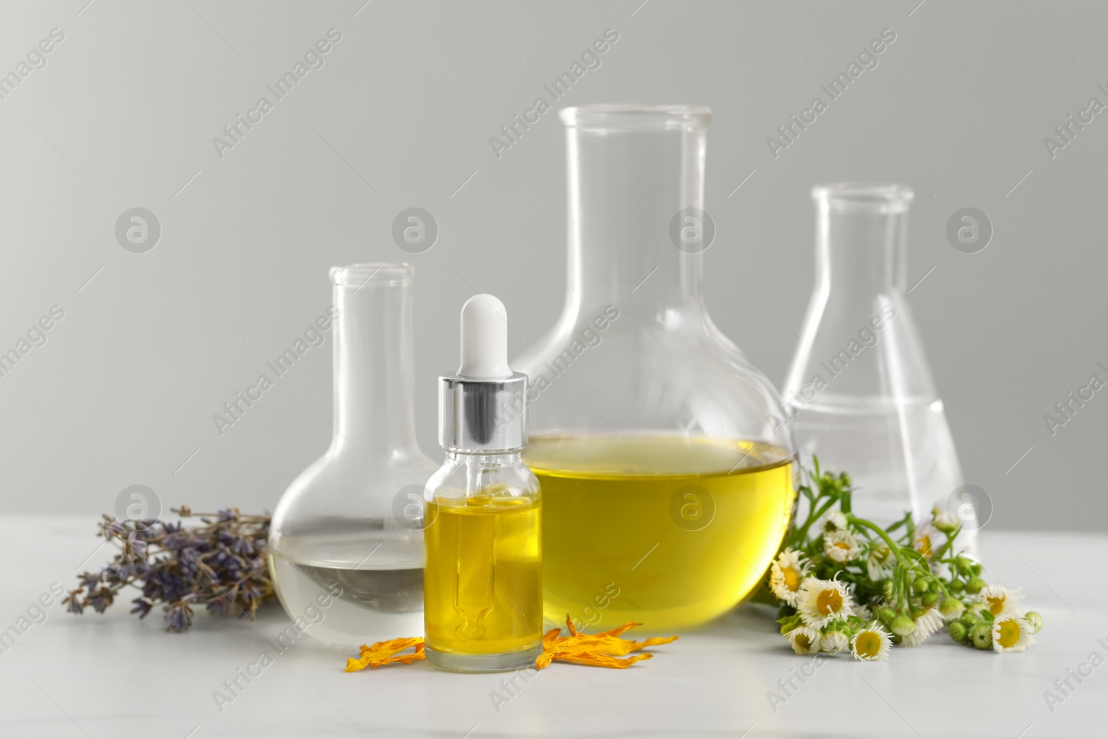 Photo of Cosmetic oil, laboratory dishware and flowers on white table