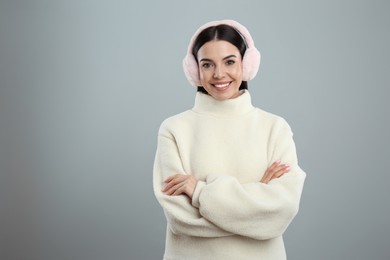 Beautiful young woman wearing earmuffs on light grey background. Space for text