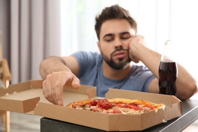 Photo of Lazy young man with pizza and drink at home