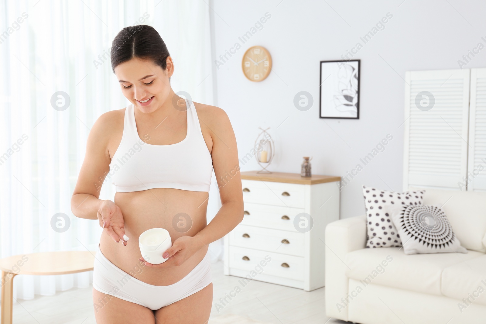 Photo of Pregnant woman holding body cream at home