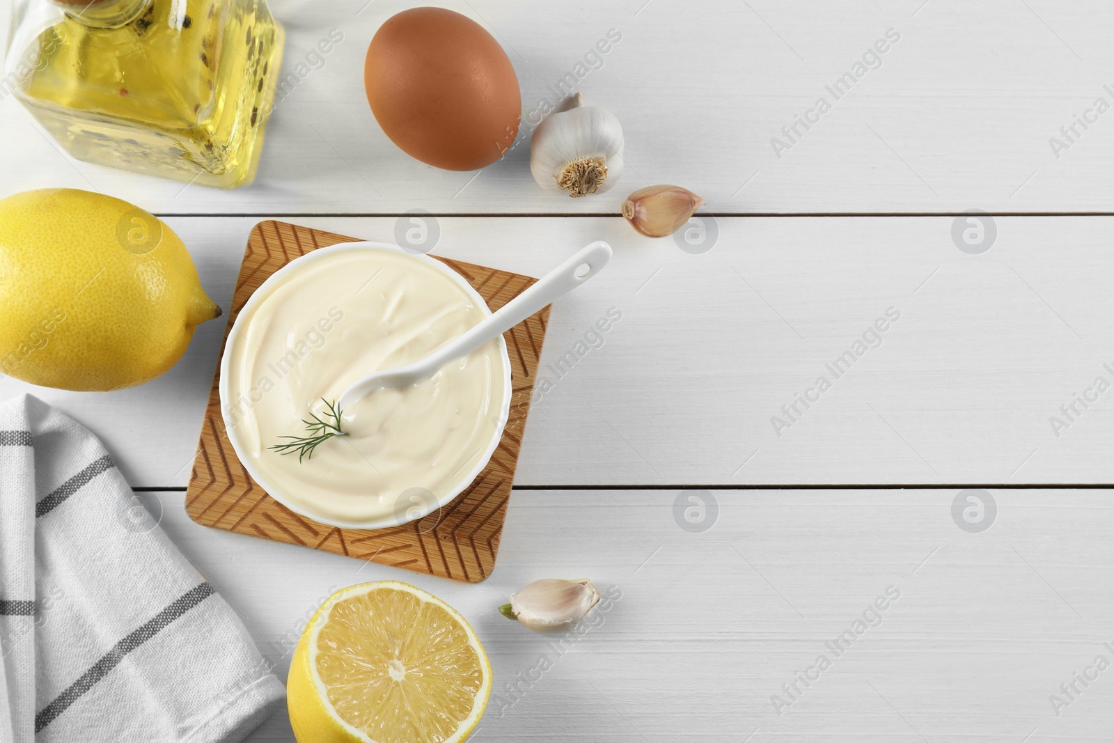 Photo of Fresh mayonnaise sauce in bowl and ingredients on white wooden table, flat lay. Space for text