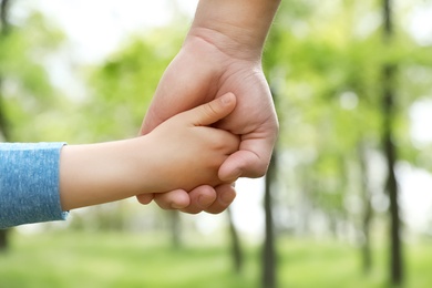 Photo of Little child holding hands with his father outdoors, closeup. Family time