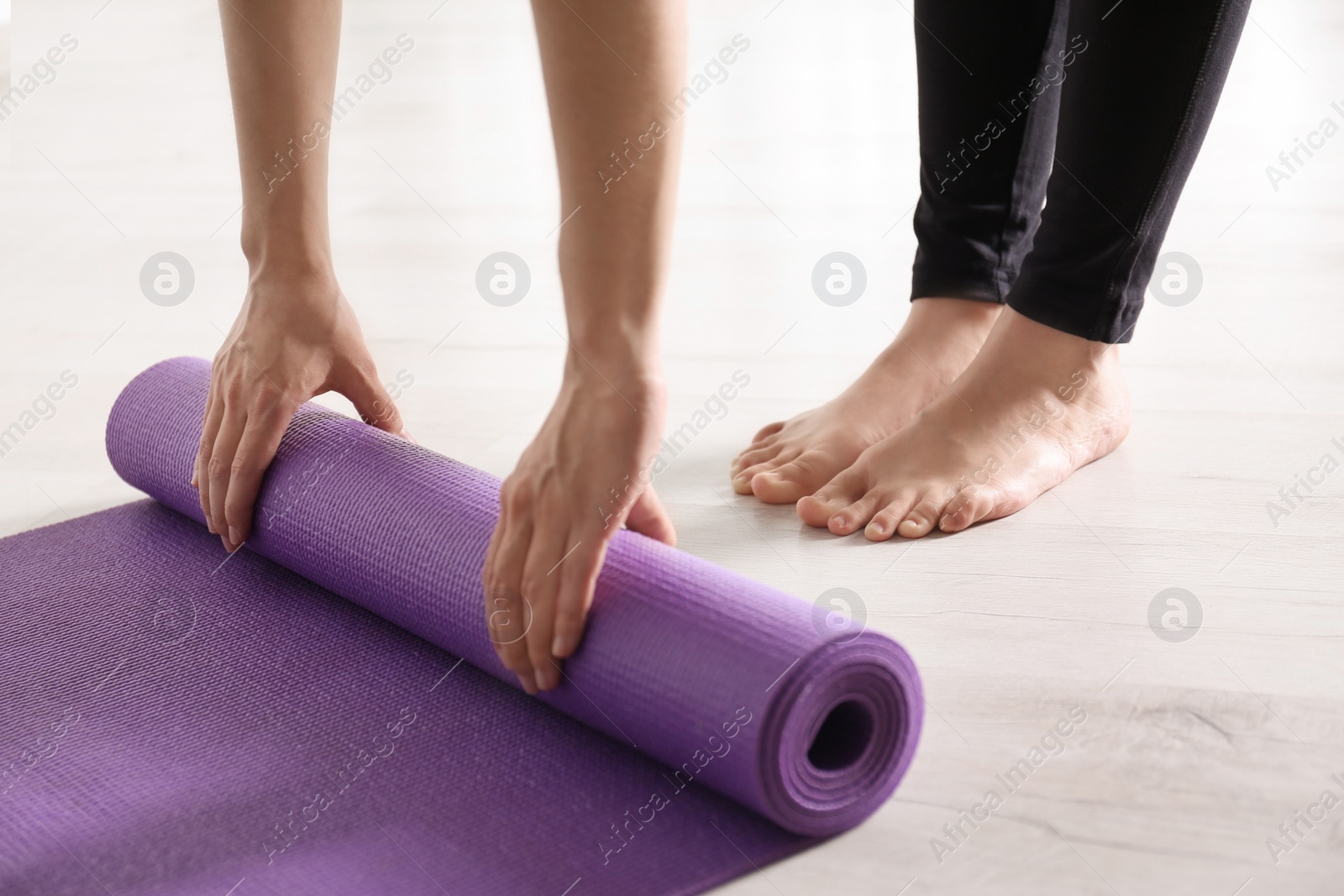 Photo of Woman rolling yoga mat on floor indoors, closeup