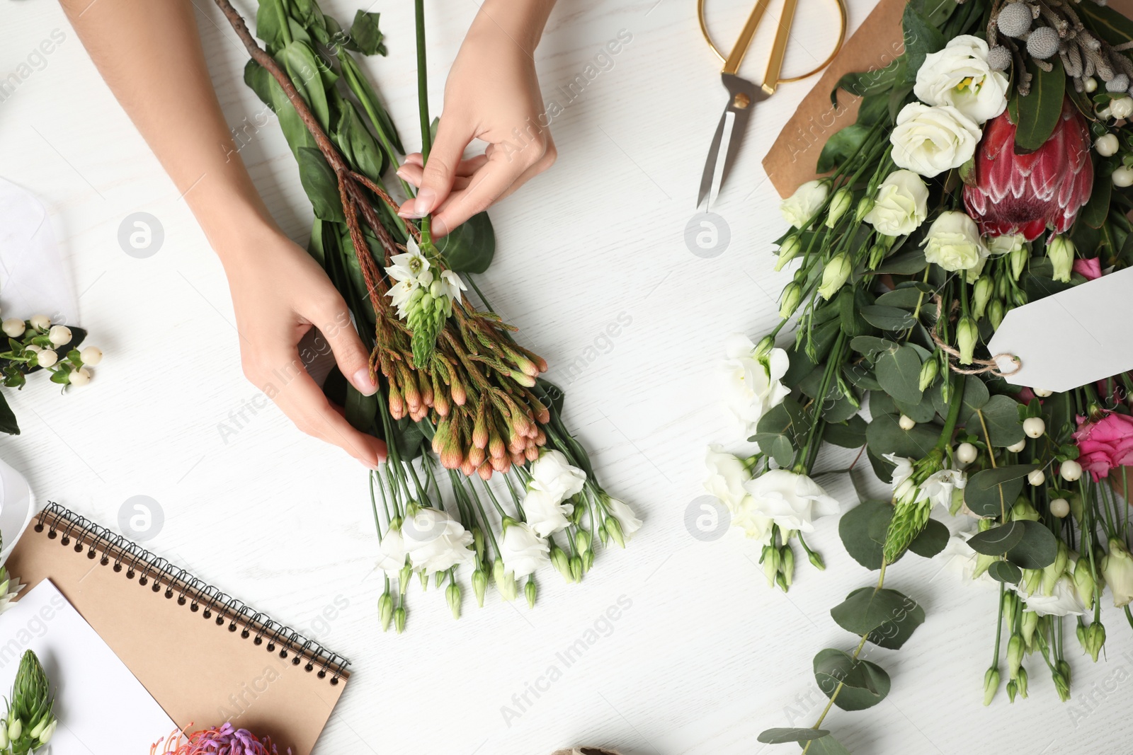 Photo of Florist making beautiful bouquet at white wooden table, top view