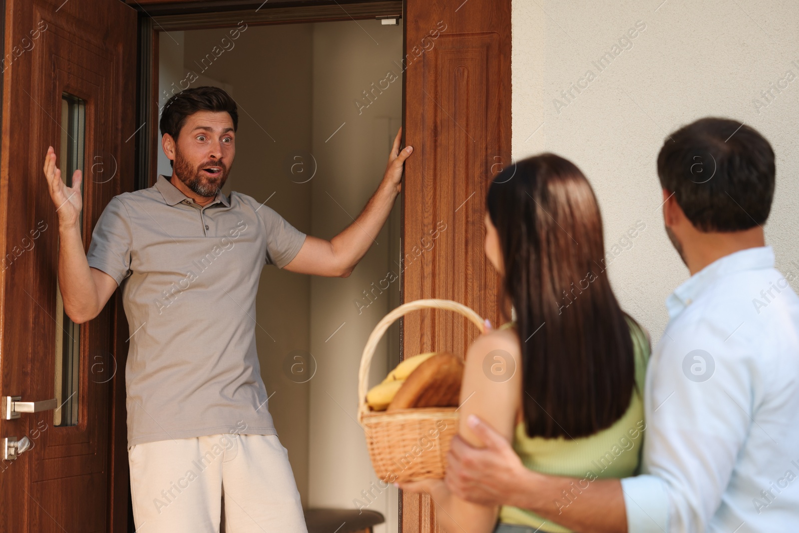 Photo of Friendly relationship with neighbours. Young couple with wicker basket of products treating shocked man outdoors