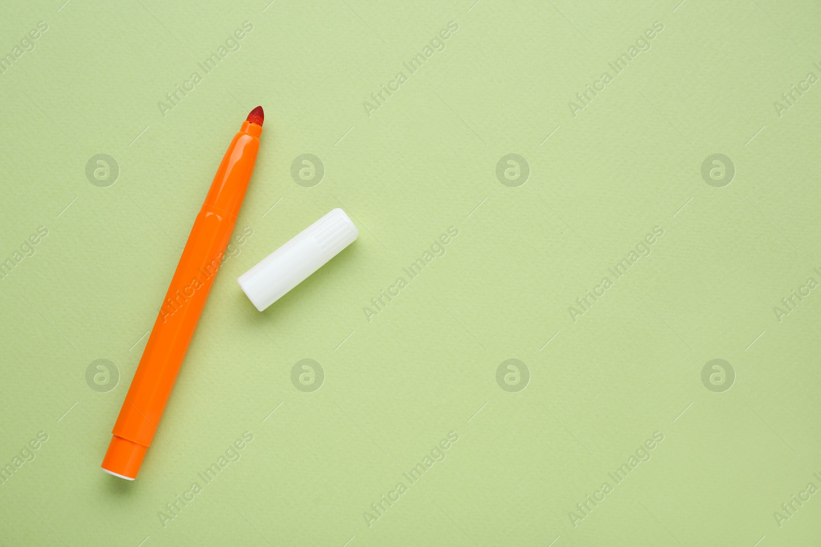 Photo of Orange marker with cap on light green background, flat lay. Space for text