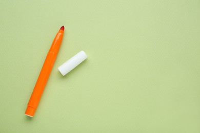 Photo of Orange marker with cap on light green background, flat lay. Space for text