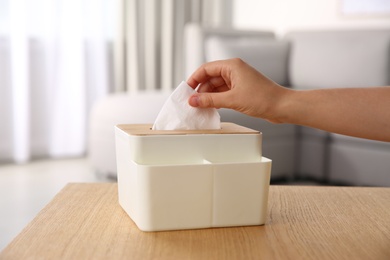 Photo of Woman taking paper tissue out of box on wooden table at home, closeup