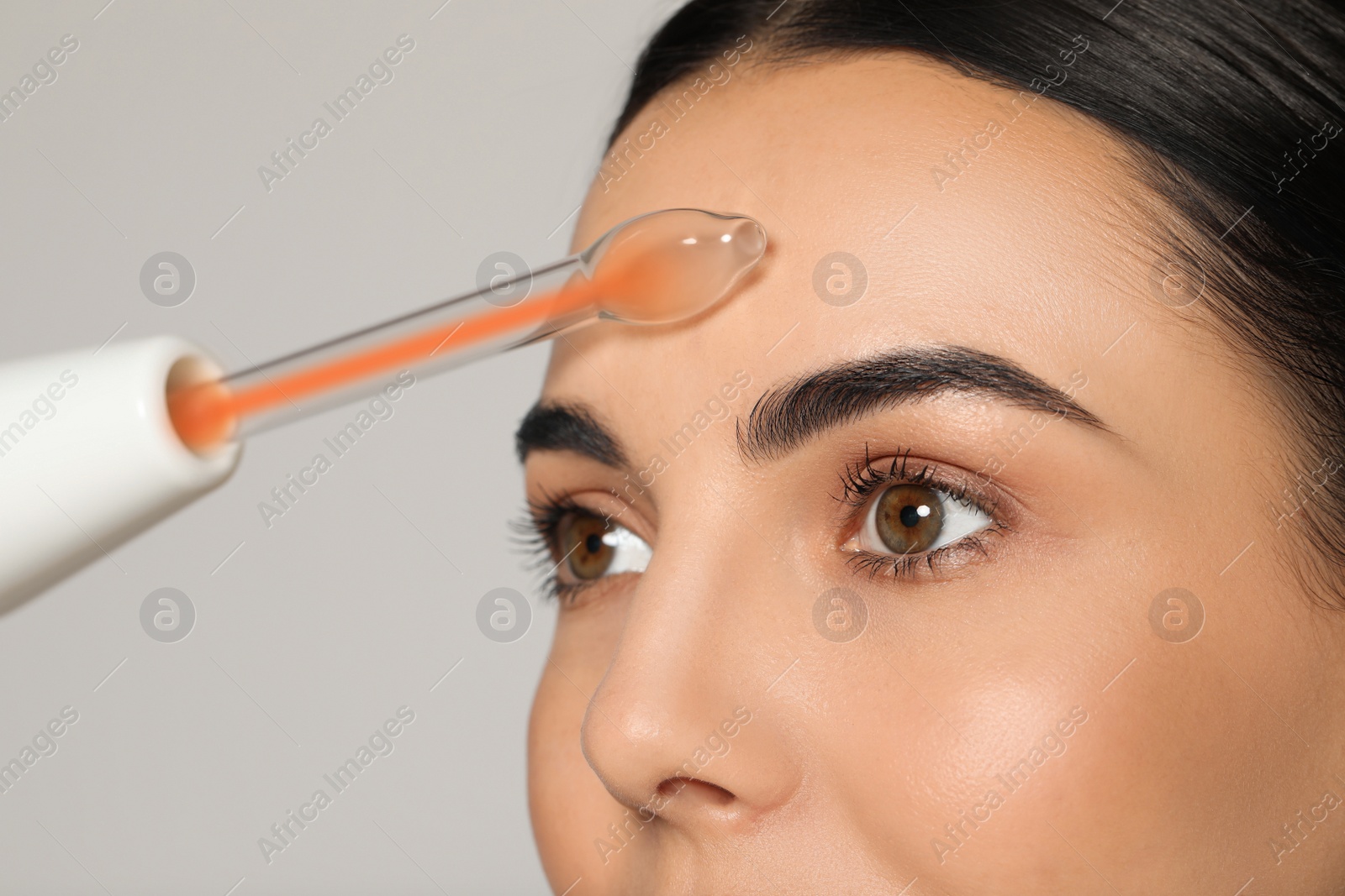 Photo of Woman using high frequency darsonval device on grey background, closeup