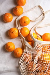 Photo of Net bag with many fresh ripe tangerines on white cloth, flat lay