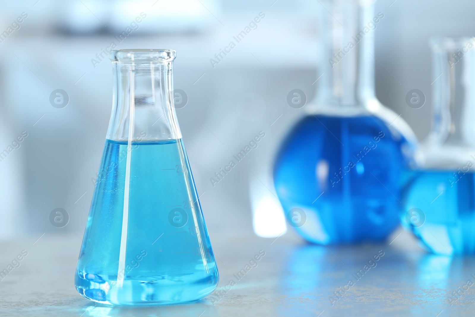 Photo of Conical flask with light blue liquid on table in laboratory. Space for text