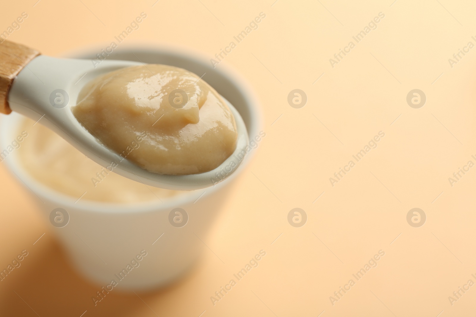 Photo of Eating healthy baby food with spoon on beige background, closeup. Space for text