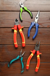 Different pliers on wooden table, flat lay