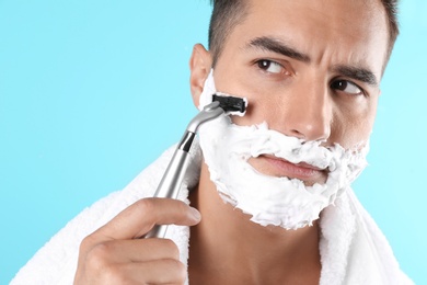 Handsome young man shaving on color background