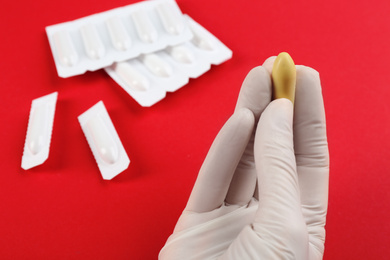 Photo of Woman holding suppository on red background, closeup. Hemorrhoid treatment