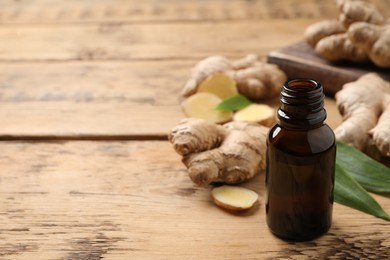 Photo of Glass bottle of essential oil and ginger root on wooden table, space for text