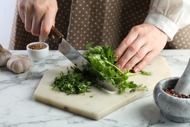 Photo of Woman cutting fresh coriander at white marble table, closeup