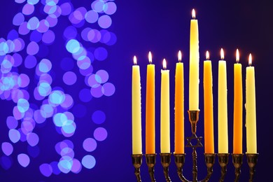 Photo of Hanukkah celebration. Menorah with burning candles on blue background with blurred lights, space for text