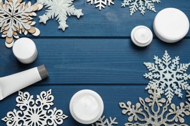 Photo of Frame of cosmetic products and snowflakes on blue wooden table, flat lay with space for text. Winter skin care