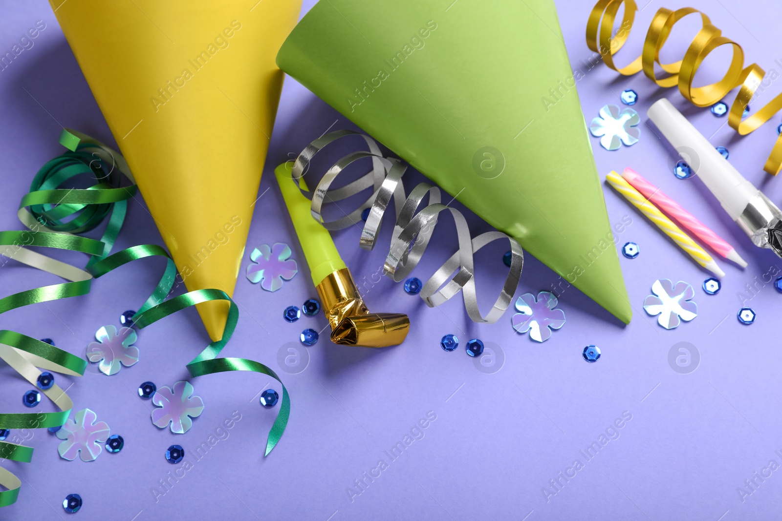 Photo of Birthday celebration. Party hats, blower, candles and decorative accessories on violet background, above view