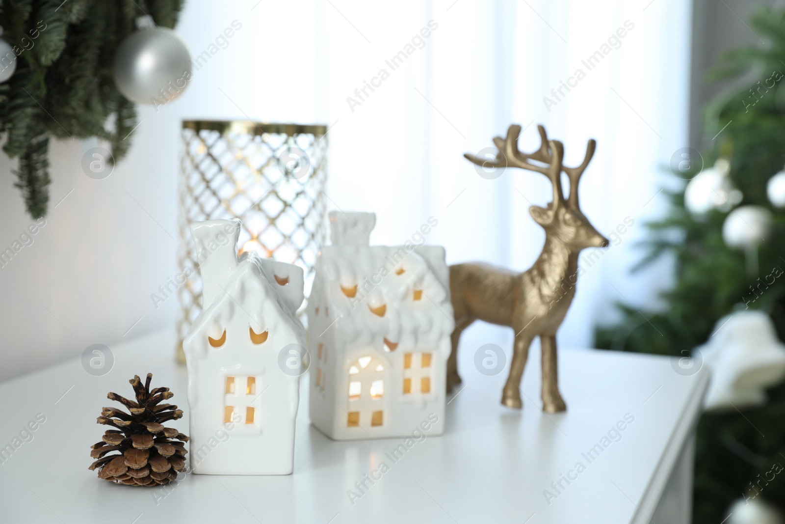 Photo of Beautiful house shaped Christmas lanterns with burning candles on commode indoors