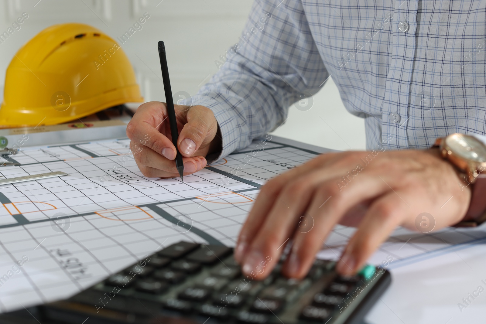 Photo of Architect working with construction drawings and calculator indoors, closeup