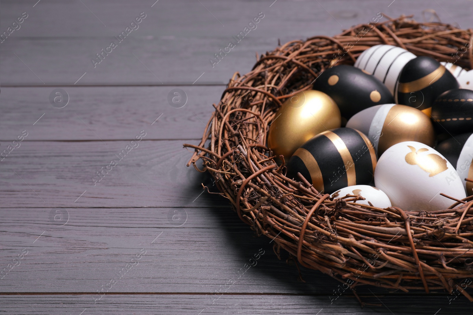 Photo of Festively decorated Easter eggs and vine wreath on grey wooden table, closeup. Space for text
