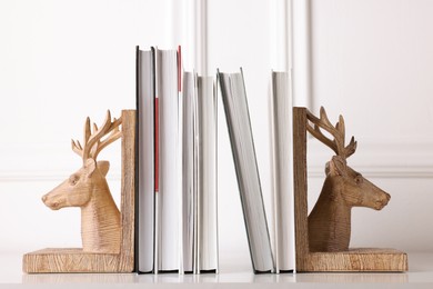 Photo of Wooden deer shaped bookends with books on table indoors