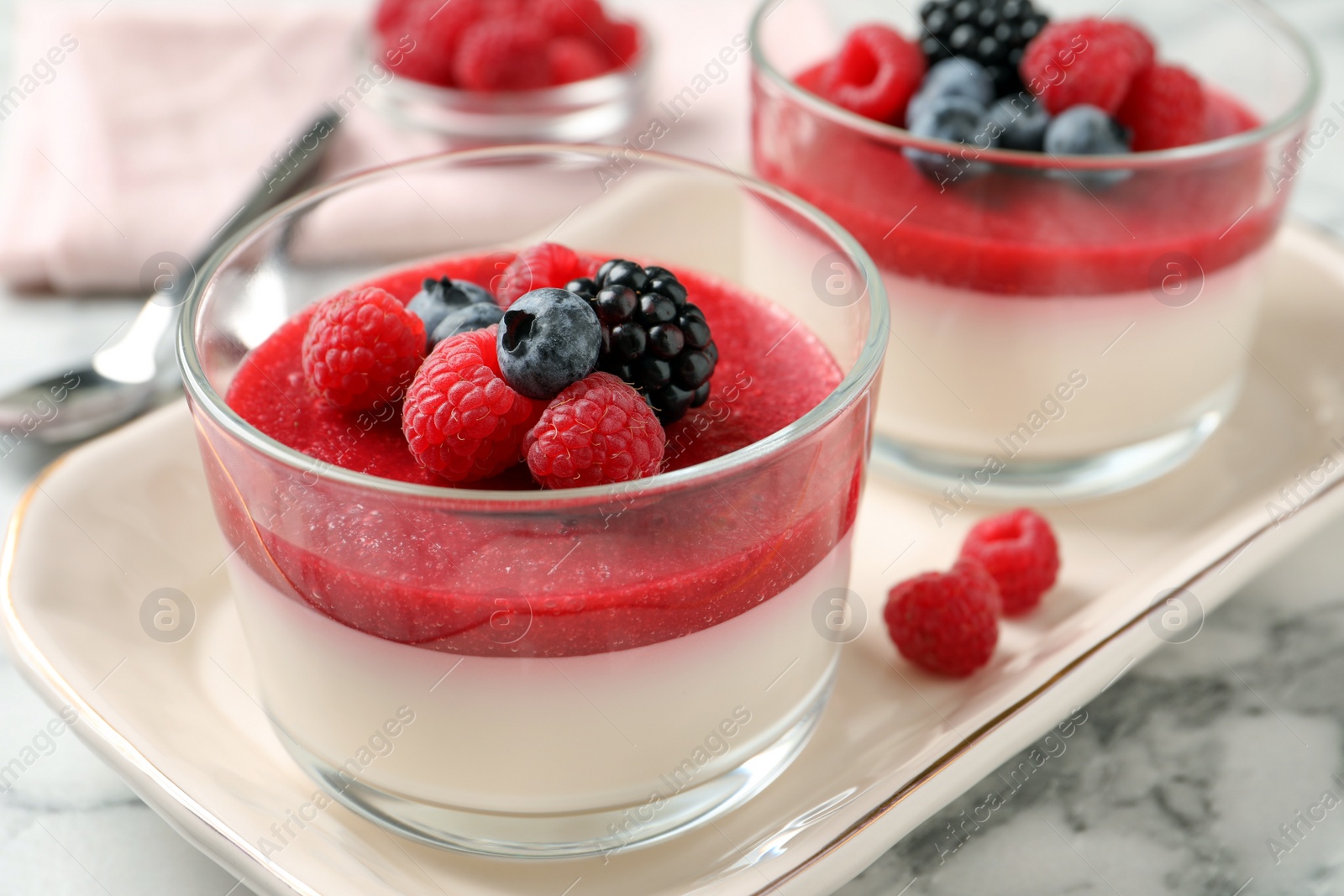 Photo of Delicious panna cotta with fruit coulis and fresh berries served on white marble table, closeup