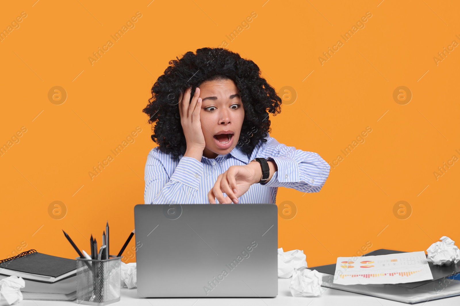 Photo of Stressful deadline. Scared woman checking time on wristwatch at white table against orange background