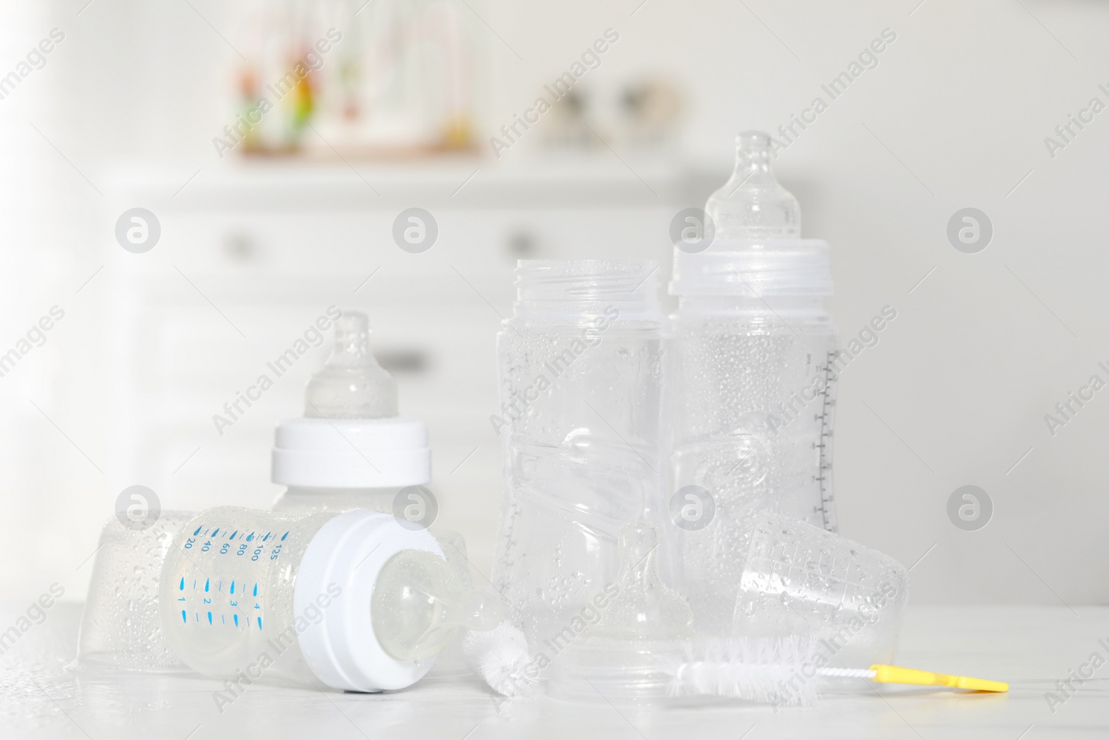 Photo of Clean baby bottles with nipples after sterilization and cleaning brush on white table indoors