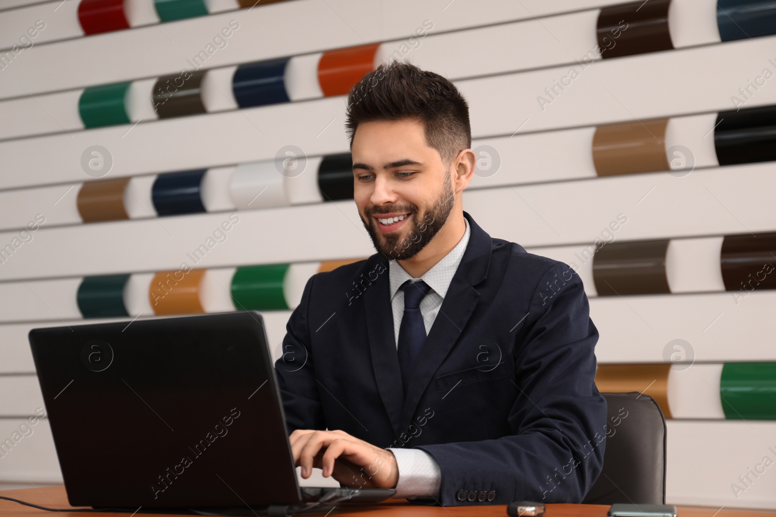 Photo of Salesman working with laptop at desk in car dealership