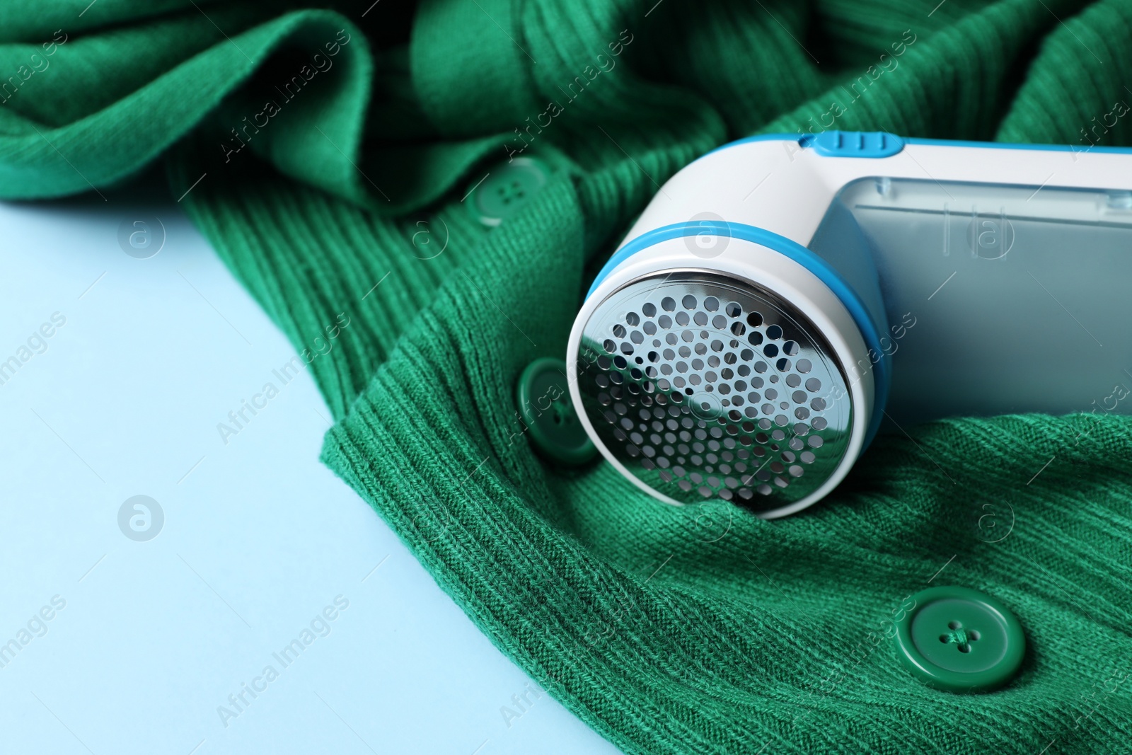 Photo of Modern fabric shaver and woolen cardigan on light blue background, closeup