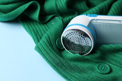 Modern fabric shaver and woolen cardigan on light blue background, closeup