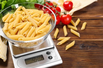 Photo of Kitchen scale with bowl of pasta on wooden table, closeup