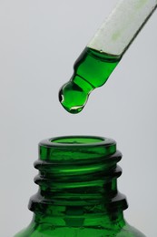 Dripping green facial serum from pipette into glass bottle on white background, closeup