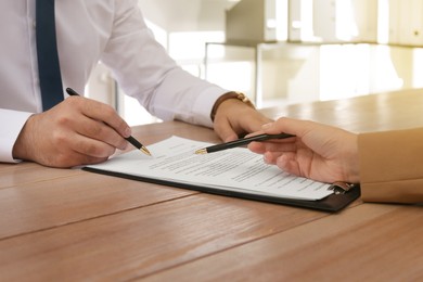Image of Man signing document at wooden table in office, closeup. Insurance concept