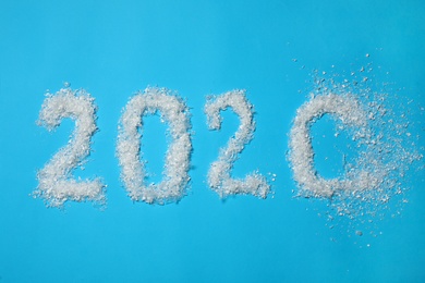 Photo of Year number 2020 made of artificial snow getting blown away on light blue background, flat lay