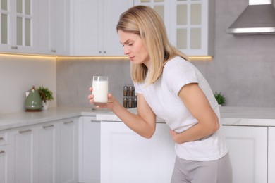 Photo of Woman with glass of milk suffering from lactose intolerance in kitchen, space for text