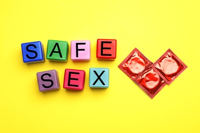 Photo of Words SAFE SEX made with colorful cubes and condoms on yellow background, flat lay