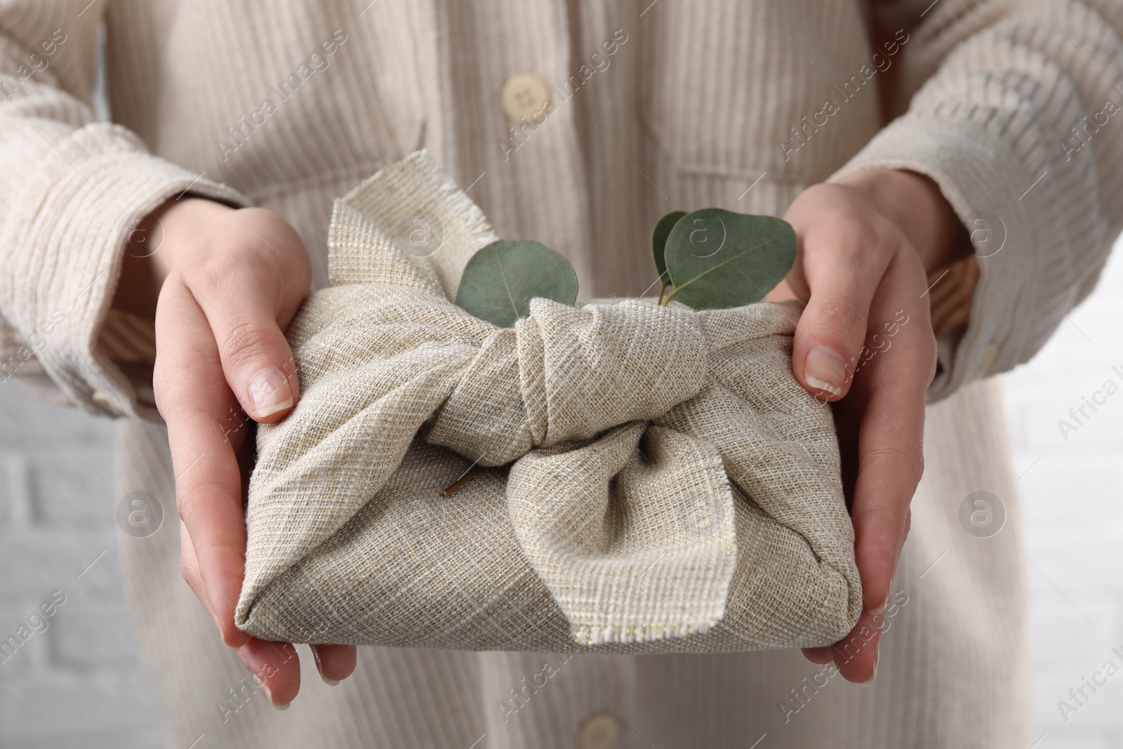 Photo of Furoshiki technique. Woman holding gift packed in fabric and decorated with eucalyptus branch, closeup