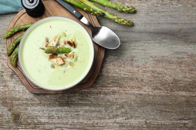 Photo of Bowl of delicious asparagus soup served on wooden table, flat lay. Space for text